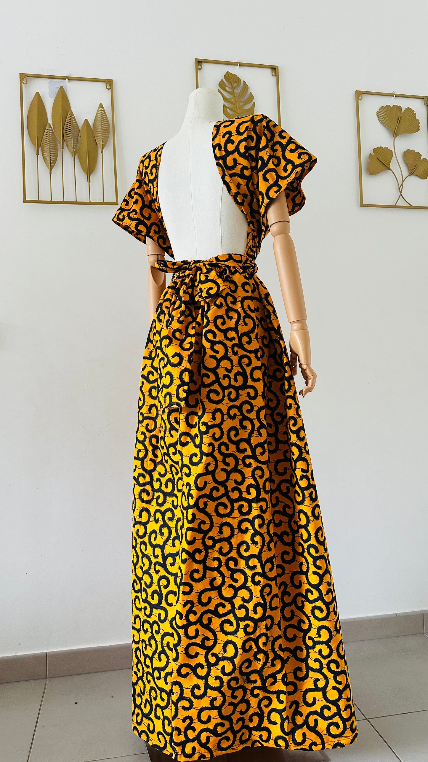 Jeune femme portant une robe Infinity en wax jaune et noir, nouée façon bustier, fond studio beige, création artisanale Kaysol Couture.